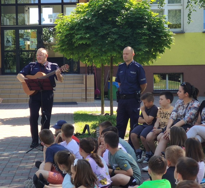 Policjanci podczas pogadanki z dziećmi. Policjant gra na gitarze.