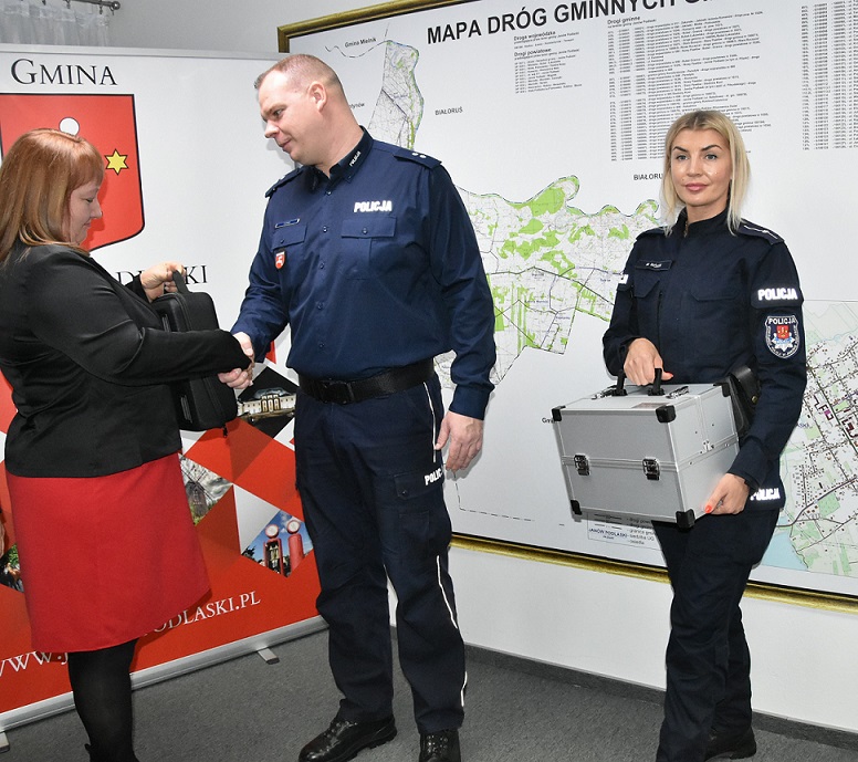 Przewodnicząca Rady Gminy przekazuje walizkę Zastępcy Komendanta Komisariatu. Po prawej stronie stoi dzielnicowa z walizką