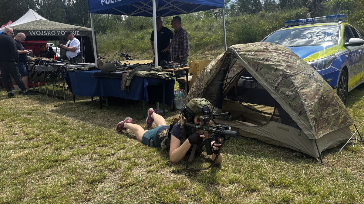 kobieta leżąca w kamizelce tatktycznej z bronią prezentowaną przez policję przy stoisku policyjnym