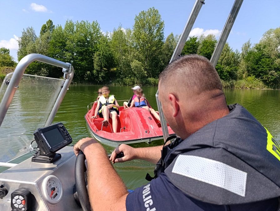 policjant rozmawia z dziećmi siedzącymi na rowerku wodnym