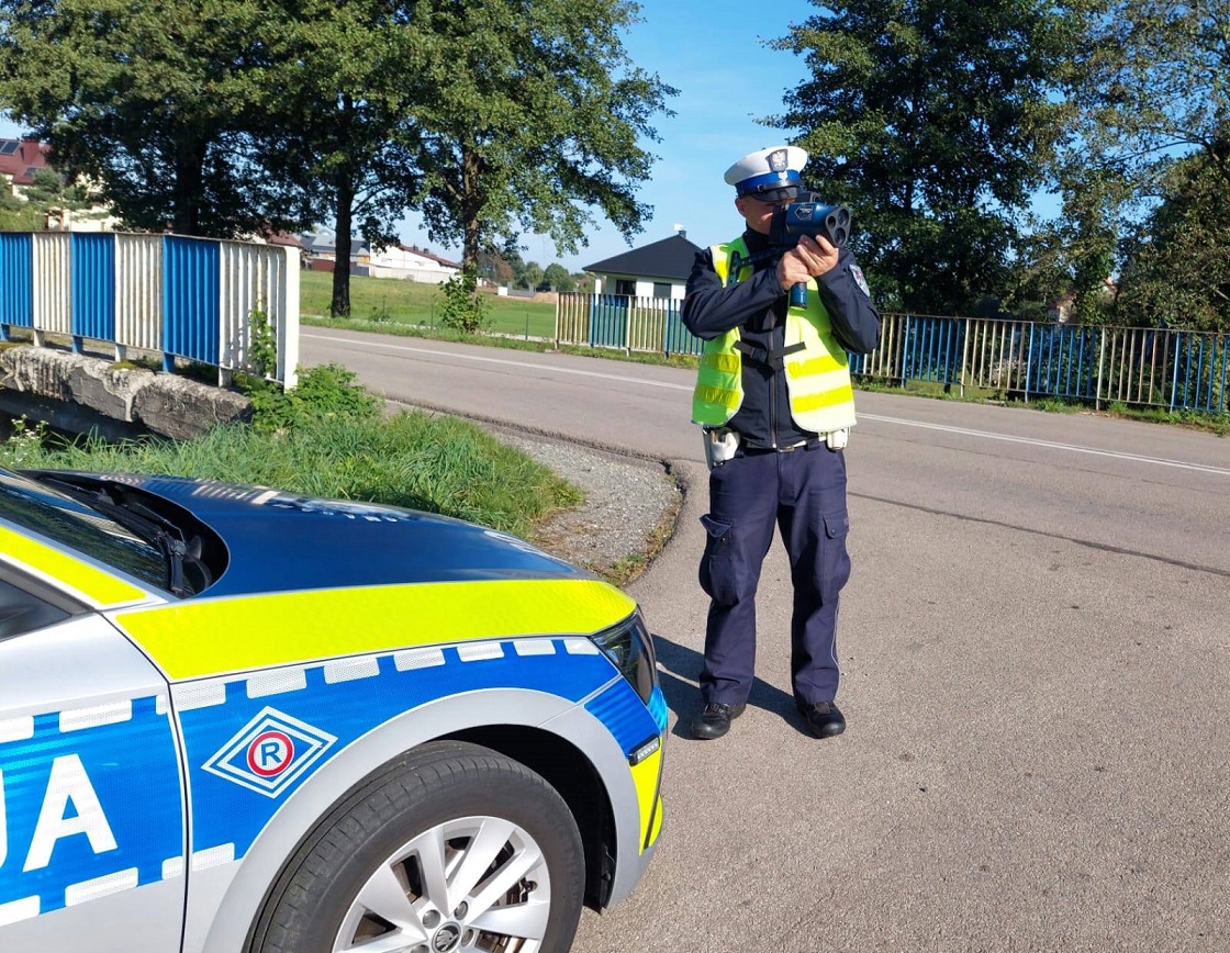 policjant stoi przy radiowozie, kontroluje prędkość za pomocą miernika prędkości