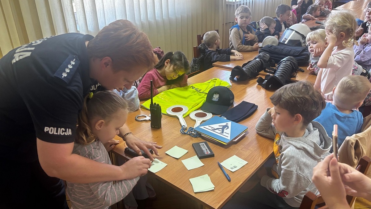 policjantka pokazuje dzieciom sposób zabezpieczania odbitek linii papilarych. Jedno z dzieci wykonuje je osobiście