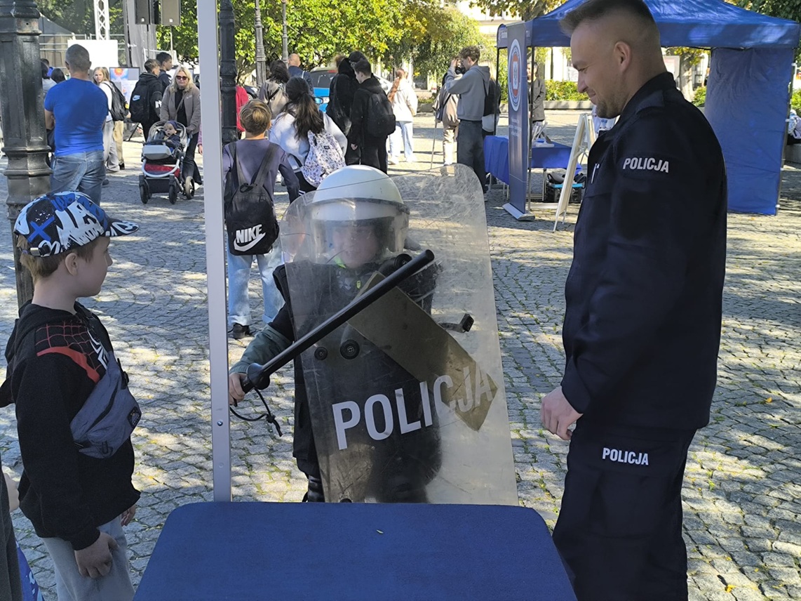 policjant stoi przy stoisku z dziećmi przymierzającymi elementy umundurowania