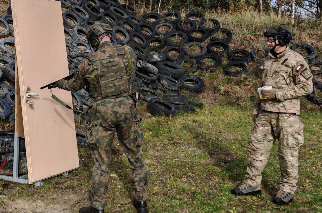 żołnierz i insrtuktor podczas szkolenia na strzelnicy. Żołnierz strzela do drzwi