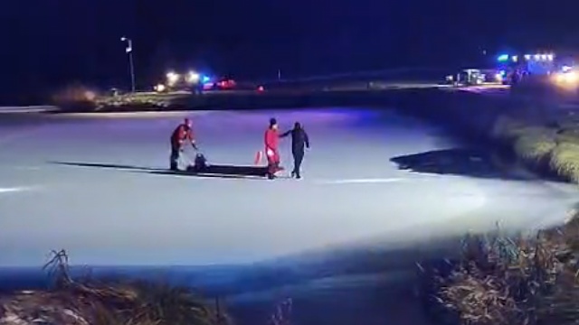 Strażacy prowadzą mężczyznę do brzegu po zamarzniętym zbiorniku wody.