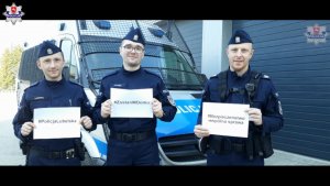 trzej policjanci trzymający w rękach kartki zz hasłami promującymi pozostanie w domu