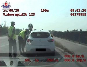 policjanci Wydziału Ruchu Drogowego prowadzący kontrolę. Jeden z nich pochyla się przed otwartymi drzwiami kierowcy auta rozmawiając z nim