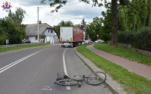 miejsce wypadku drogowego. Leżący na ulicy rower za nim uszkodzony samochód