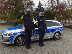 policjanci stojący przy radiowozie i oddający honor