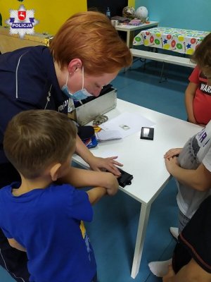 policjantka pokazuje dzieciom w jaki sposób zabezpiecza się odbitki linii papilarnych