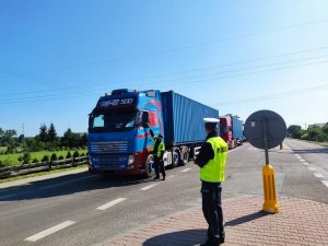policjant prowadzący kontrolę drogową samochodu ciężarowego. drugi funkcjonariusz stoi na chodniku