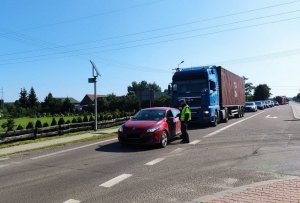 policjant stoi przy samochodzie osobowym, prowadzi kontrolę drogową