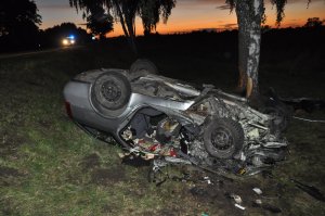 uszkodzony nissan leżący na dachu poza drogą publiczną , w tle światła radiowozu