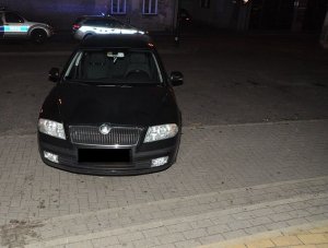 samochód marki Skoda, który stoi na parkingu, za nim w tle dwa policyjne radiowozy