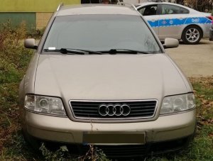 samochód marki audi stojący na podwórku. Za nim w tle widoczny fragment radiowozu