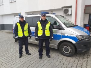 dwaj umundurowani policjanci stoją przy radiowozie