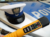 czapka policjanta Wydziału Rchu Drogowego oraz rządzenie alcoblow leżące na mace oznakowanego radiowozu