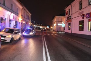 samochód koloru białego, za nim stojący radiowóz, w tle widoczne oznakowane przejście dla pieszych