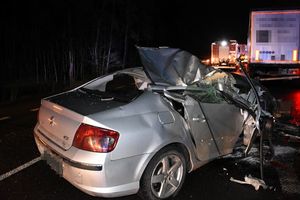 uszkodzony samochód peugeot stojący na ulicy, za nim samochód ciężarowy. W tle dwa wozy straży pożarnej.