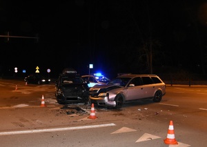 dwa uszkodzone samochody stojące na skrzyżowaniu. W tle radiowóz z włączonymi światłami.