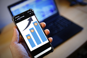 telefon trzymany w ręku na którym widoczny jest wskaźnik wzrostu zysków z krypto waluty