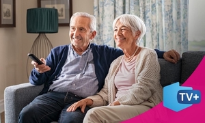 dwoje seniorów siedzi na kanapie. Mężczyzna trzyma pilot w ręku