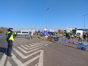 stojący policjanci, za nimi radiowóz, po drugiej stronie widoczne miejsce protestu