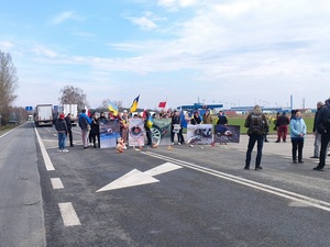 uczestnicy protestu stojący z transparentami na pasie drogi