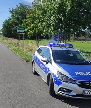 radiowóz, za nim tabliczka z nazwą miejscowości