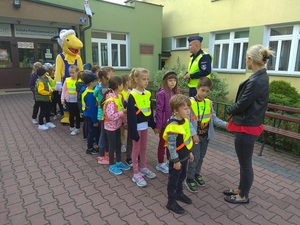 grupa dzieci stojąca z policjantami i opiekunem przed szkołą