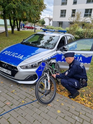 policjant podczas znakowania roweru. W tle radiowóz