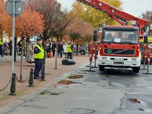 POLICJANT ZABEZPIECZA MIEJSCE ZDARZENIA. W TLE INNE SŁUŻBY I OSOBY KTÓRE WYSZŁY Z URZĘDU.