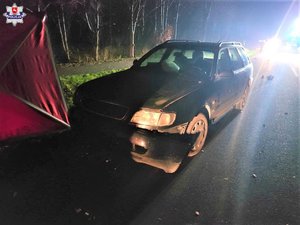 miejsce wypadku. Stojący na ulicy samochód. Przed nim fragment parawanu