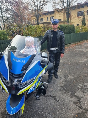dzieci siedzą za kierownicą motocykla. Obok stoi policjant