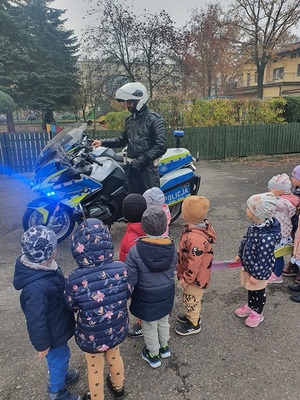 policjant stoi przy motocyklu obok stoją przedszkolaki