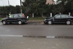 dwa samochody stojące na ulicy. Przy pierwszym stoi policjant