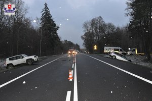 miejsce wypadku drogowego. Dwa uszkodzone auta stojące poza drogą. W tle służby ratunkowe