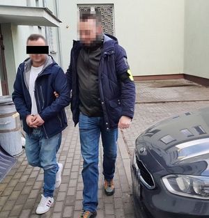 policjant doprowadza zatrzymanego mężczyznę