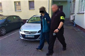 policjant doprowadza zatrzymanego mężczyznę