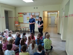 policjantka i stojąca obok opiekunka. Naprzeciw siedzące dzieci
