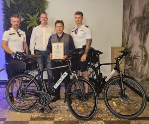 grupa osób z rowerem, policjanci i osoby uczestniczące