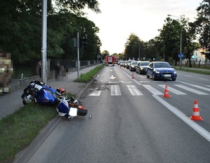 motocykl leżący na ulicy. Po drugiej stronie samochody