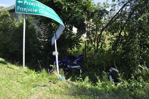 motocykl leżący na poboczu, przed nim uszkodzony znak drogowy