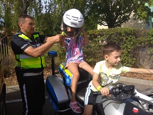 policjant przy motocyklu pomaga dziewczynce założyć hełm