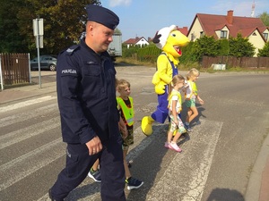 policjant z dziećmi i maskotką mrówki przechodzi przez przejście dla pieszych