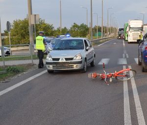 miejsce wypadku rower leżący na ulicy. Obok samochód uczestniczący w zdarzeniu oraz policjant wykonujący czynności.