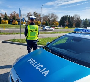 policjant stoi przy radiowozie kontroluje bezpieczeństwo na drodze