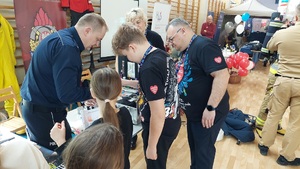 policjant pokazuje  odwiedzającym stoisko sposób zabezpieczania linii papilarnych