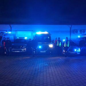 policjanci oraz funkcjonariusze innych służb stoją przy pojazdach z włączonymi sygnałami świetlnymi