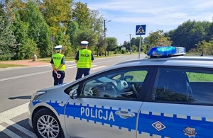 policjant i policjantka stojąca przed radiowozem policyjnym